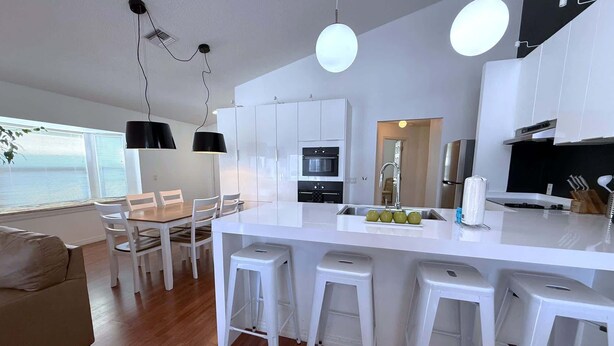 A modern kitchen with white cabinetry, a central island with stools, and a dining area with a wooden table and white chairs.