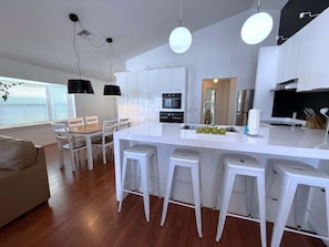 Une cuisine moderne avec des meubles blancs, un îlot central doté de tabourets et un coin repas avec une table en bois et des chaises blanches.