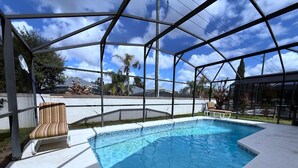 An outdoor swimming pool with a glass enclosure, surrounded by a white deck and a lounge chair. - Memory Maker Villa (Haines City)