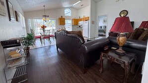 A modern living room with a dark leather sofa, a dining area with a chandelier, and a kitchen with wooden cabinets. - Memory Maker Villa (Haines City)