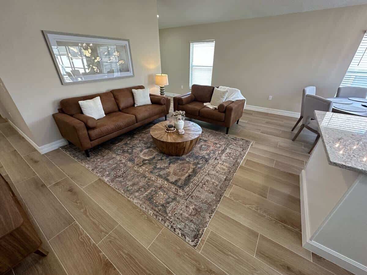 A spacious living room with a brown sectional sofa, a round coffee table, and a patterned rug.