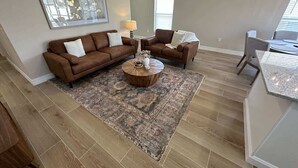 A spacious living room with a brown sectional sofa, a round coffee table, and a patterned rug. - Family Fun Fairway Villa (Haines City)