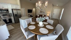 A modern kitchen with white cabinetry, stainless steel appliances, and a dining area with a round wooden table and white chairs. - Family Fun Fairway Villa (Haines City)