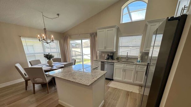 A modern kitchen with a central island, white cabinetry, and a stainless steel refrigerator. - Family Fun Fairway Villa (Haines City)