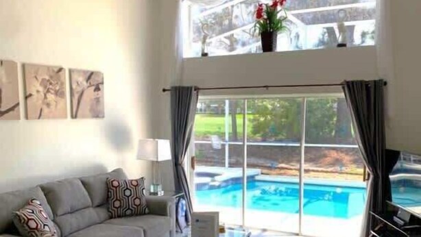 Un salon spacieux avec un canapé gris, une table basse et une grande fenêtre donnant sur une piscine.