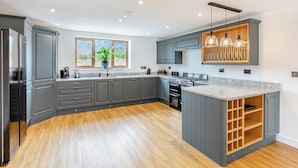 A modern kitchen with grey cabinetry, a wooden floor, a built-in oven, and a window with a view. - 5 bedroom accommodation in Belper (Belper)
