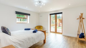 A bedroom with a bed, a chair, a wooden floor, a window, and a door leading to an outdoor area. - 5 bedroom accommodation in Belper (Belper)