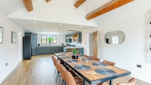 A modern kitchen with dark cabinets, a wooden dining table with leather chairs, and a large mirror on the wall. - 5 bedroom accommodation in Belper (Belper)