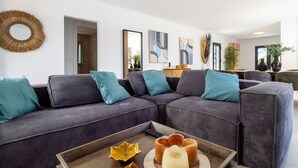 A modern living room with a sectional sofa, a coffee table, and decorative items. There are framed artworks on the wall and a potted plant in the corner.