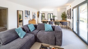 A modern living room with a sectional sofa, a dining area, and large windows.
