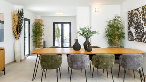 A modern dining area with a wooden table, four upholstered chairs, and two large vases with plants.