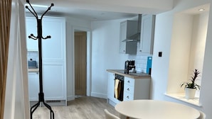 A modern kitchen with white cabinets, a built-in oven, and a coffee machine. There is a round dining table with four chairs. - Bay View House (Bangor)