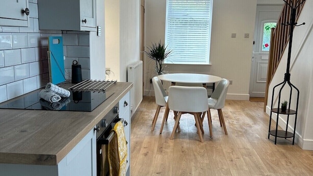 A modern kitchen with white cabinets, a wooden countertop, and a dining area with a white table and chairs. - Bay View House (Bangor)