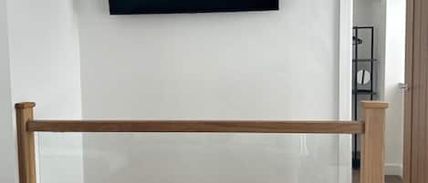 Une pièce avec un téléviseur fixé au mur, un plancher en bois et une porte visible donnant sur une autre pièce.