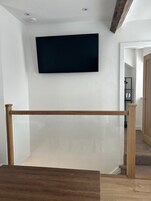 Una habitación con un televisor montado en la pared, piso de madera y una puerta visible que da a otra estancia.