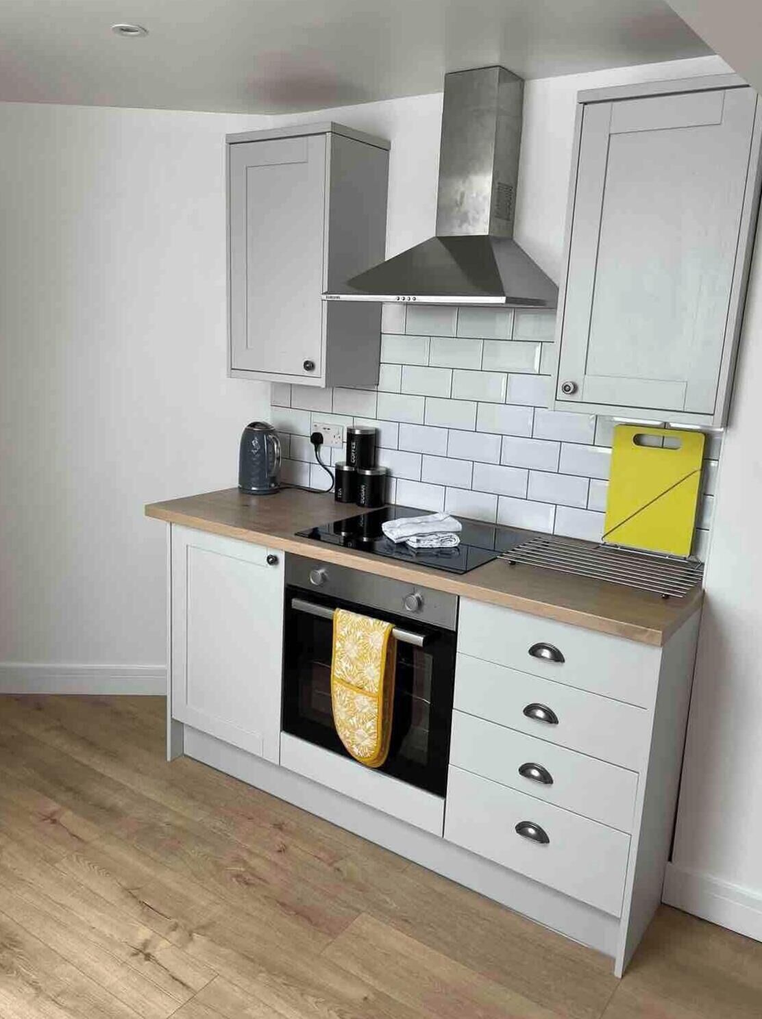 A compact kitchen with white cabinets, a stainless steel range hood, a built-in oven, and a wooden countertop.