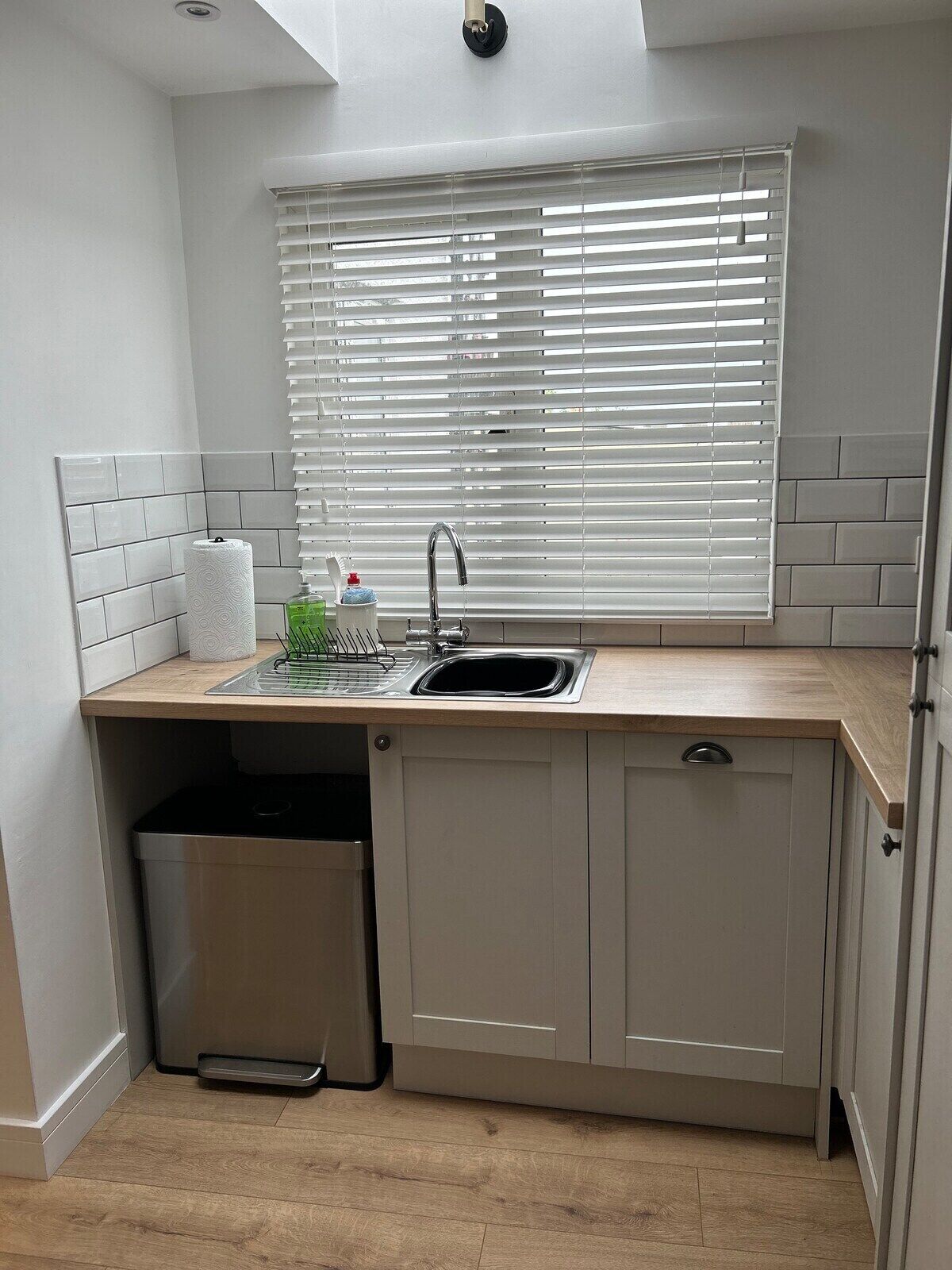 A compact kitchen with a built-in sink, a dish rack, and a trash bin.