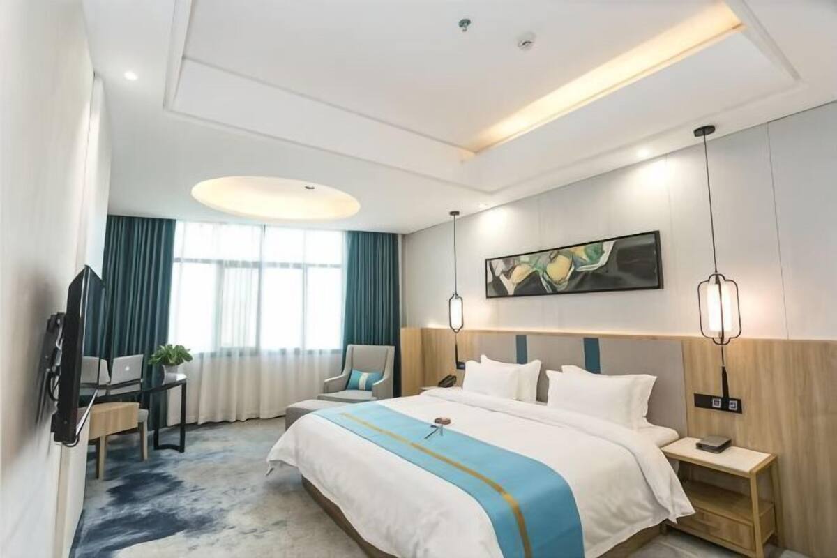 A hotel room with a large bed, bedside tables, a desk with a chair, a TV, and a painting on the wall.