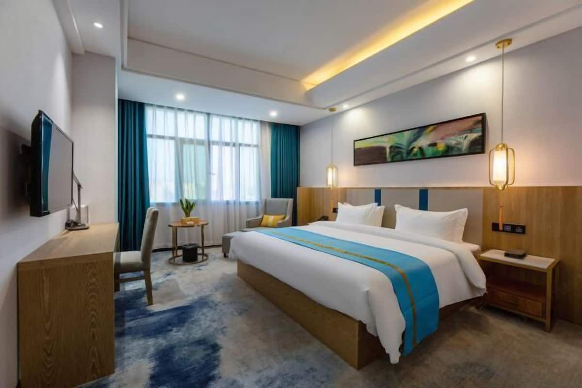 A modern hotel room with a large bed, a desk, a chair, and a TV.