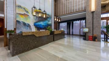 A hotel reception area with a marble wall, a reception desk, and a large abstract painting.