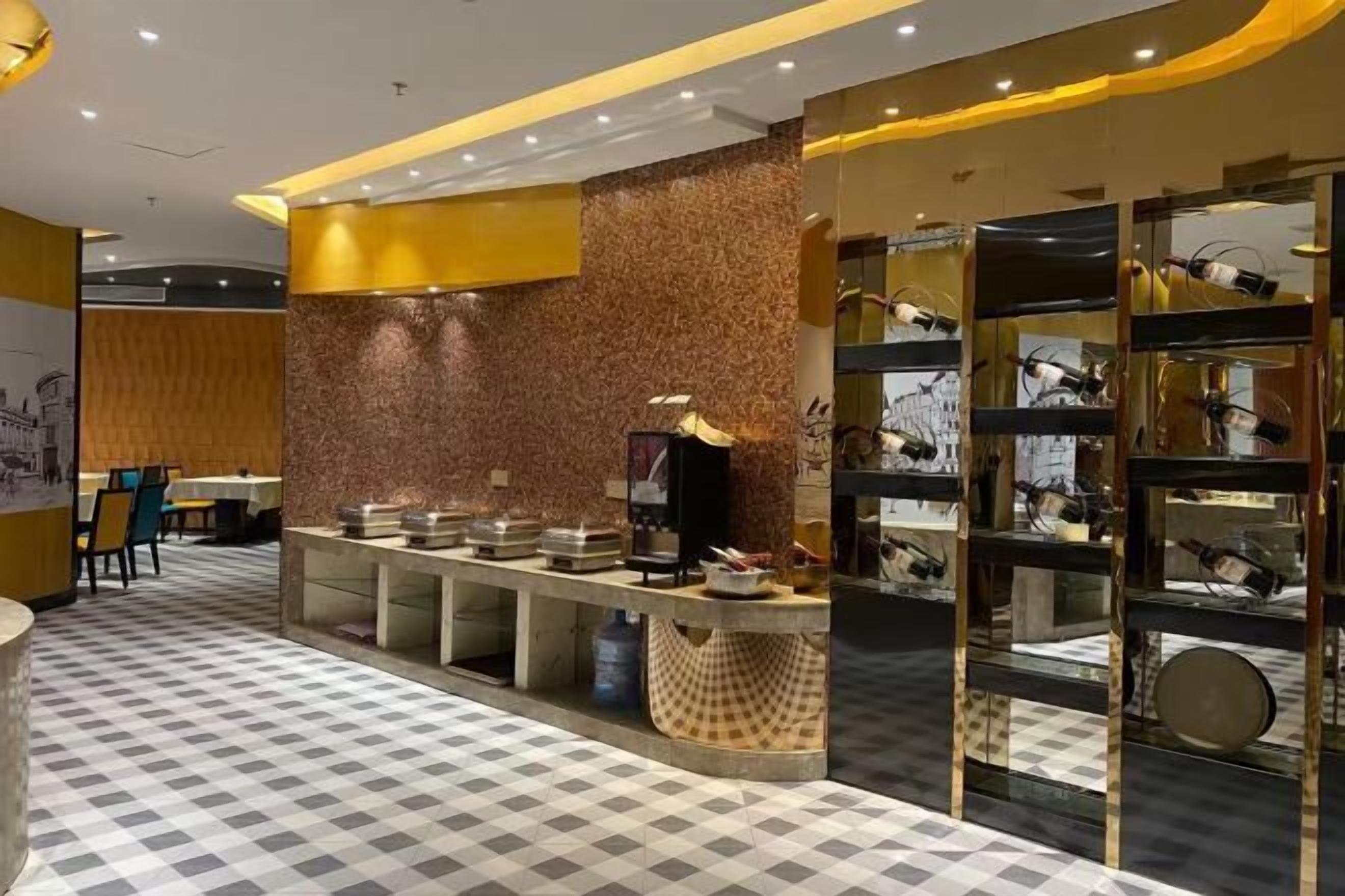 En modern hotellobby med ett rutmönstrat golv, ett område med en buffé med olika sorters mat och en utställning av köksredskap.