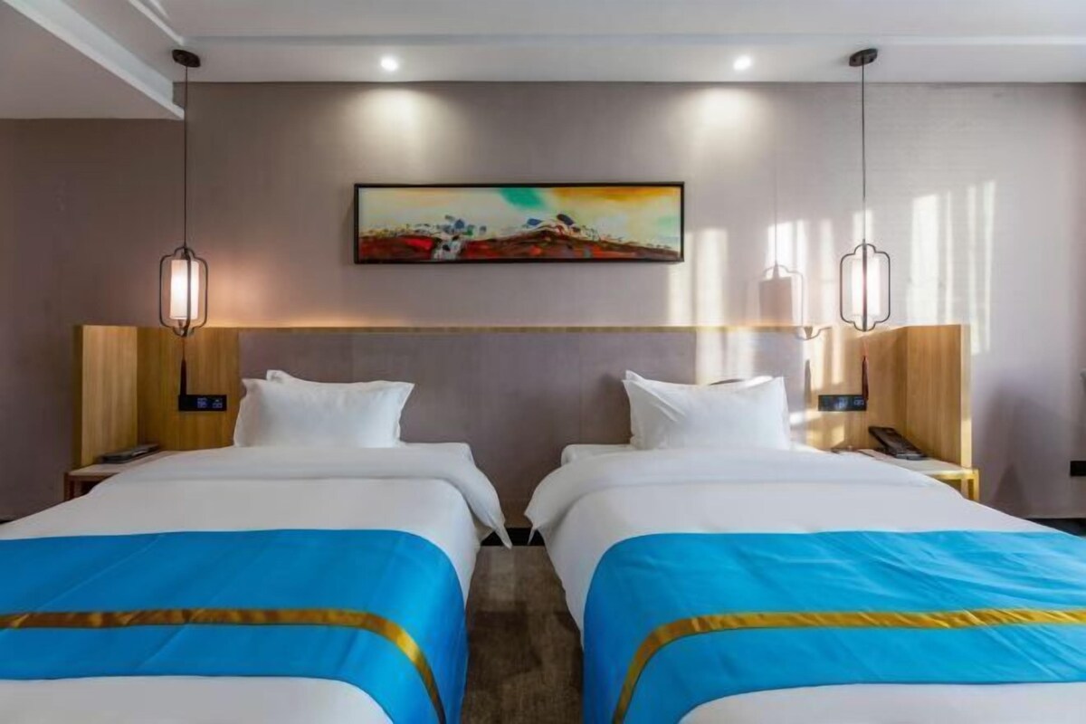 Una habitación de hotel con dos camas, un cuadro en la pared y lámparas colgantes.