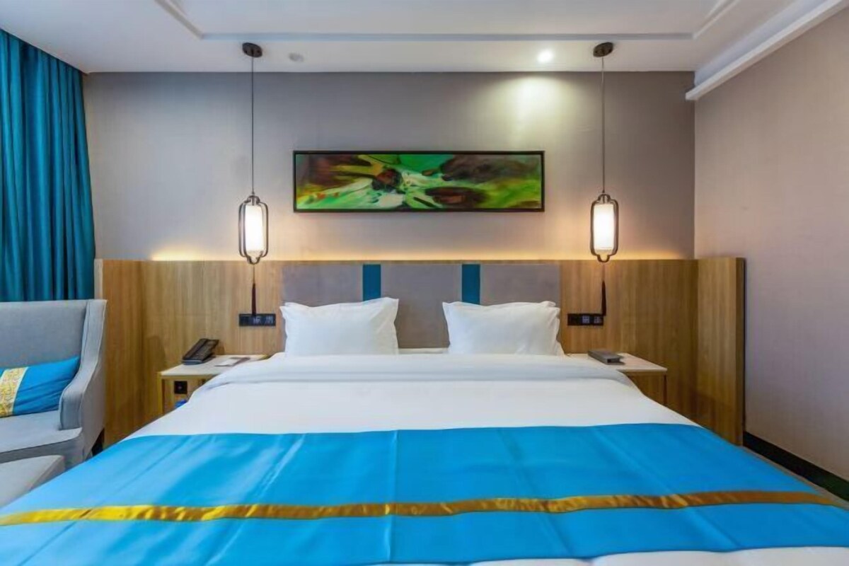 Una habitación de hotel con una cama grande, dos mesitas de noche, una silla y un cuadro en la pared.