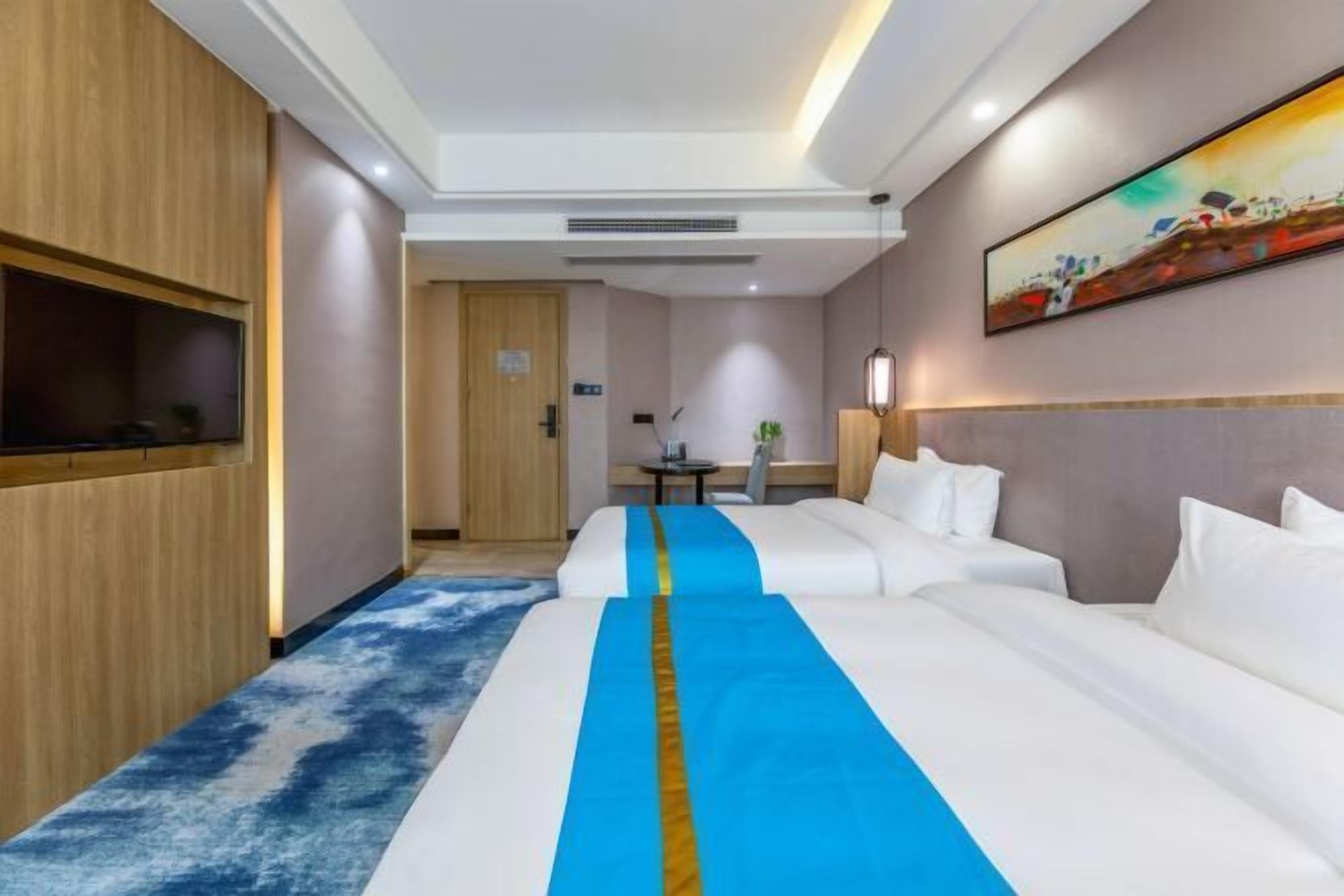 A hotel room with a large bed, a desk, a chair, and a painting on the wall.