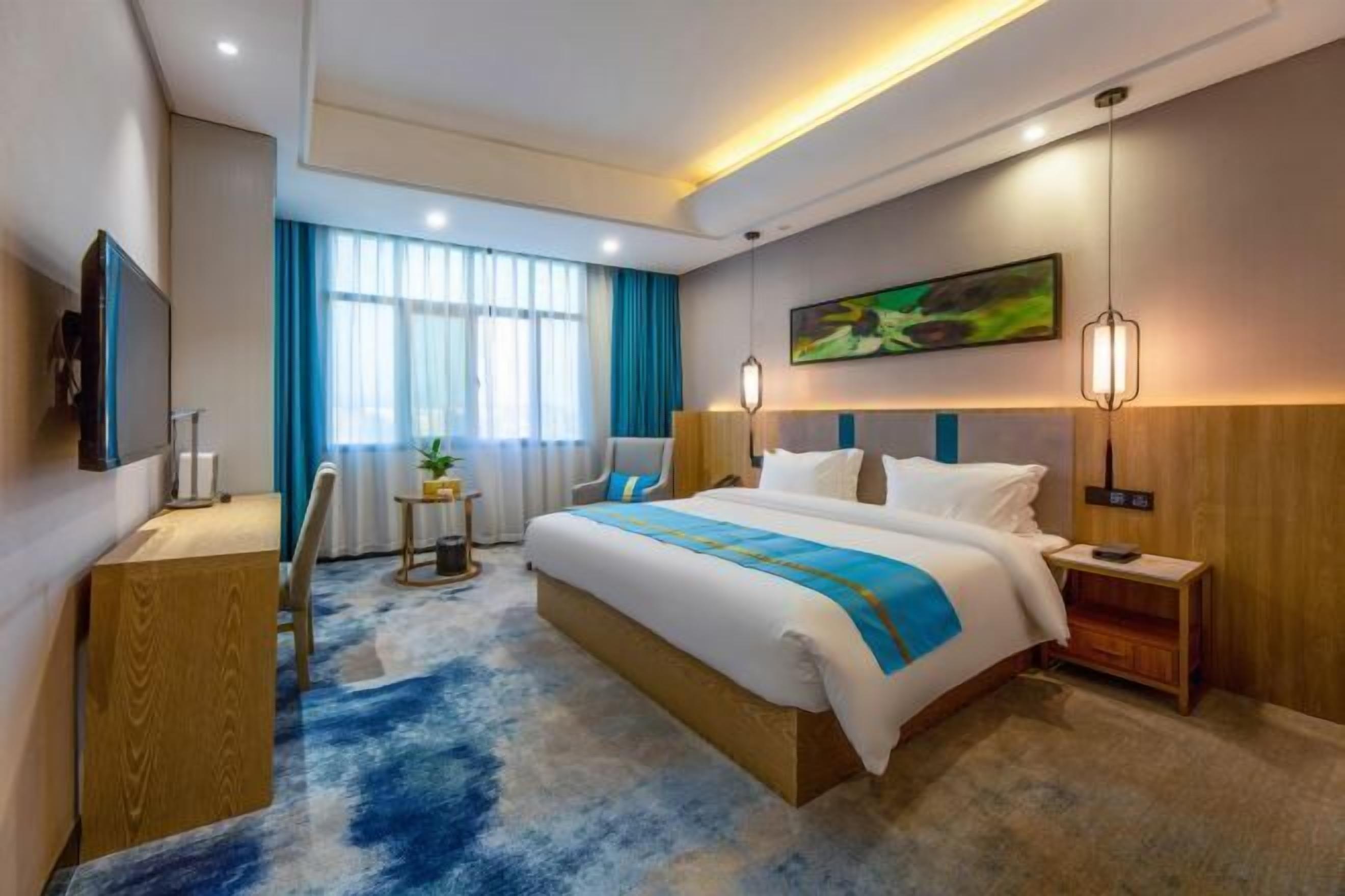 A modern hotel room with a large bed, a desk, a TV, and a window with curtains.