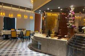 Un vestíbulo de hotel con mostrador de recepción, zona de estar y plantas decorativas.