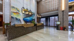 Un moderno vestíbulo de hotel con un mostrador de recepción, un mural abstracto y una escalera.