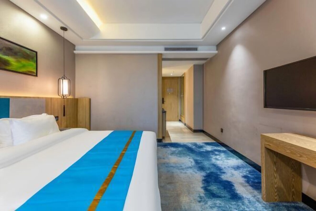 Habitación de hotel con cama, escritorio, silla, televisión y un pasillo que conduce a otra habitación.