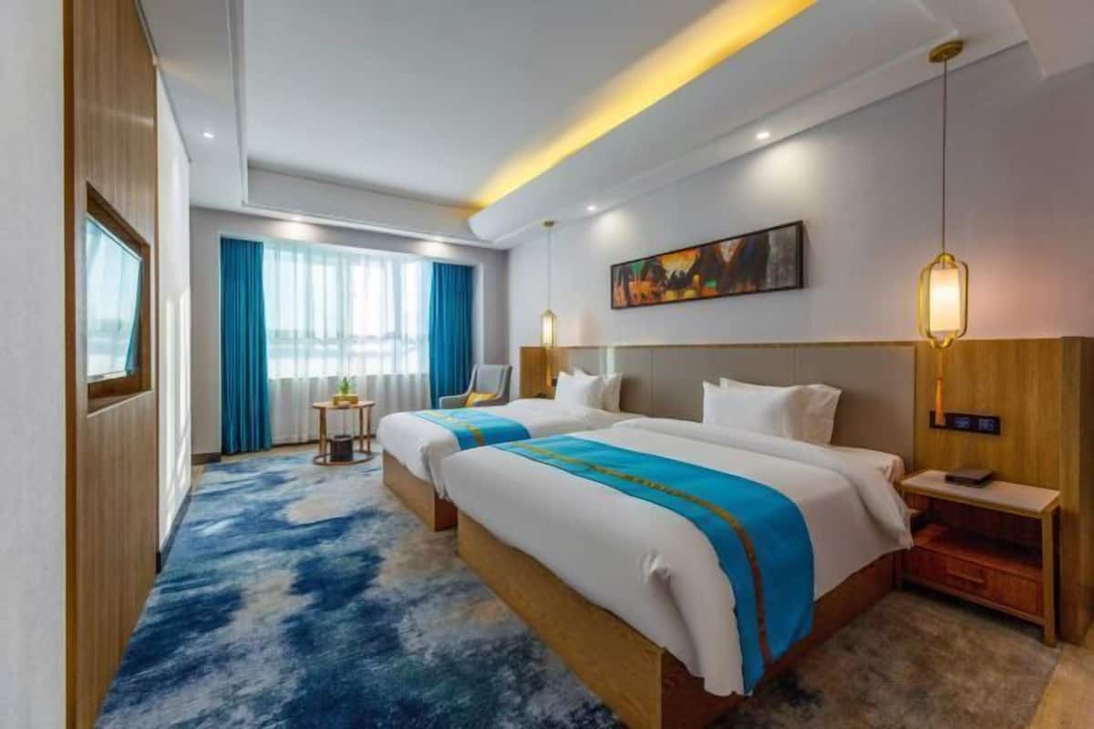 A hotel room with two beds, a large window with curtains, a painting on the wall, and a blue carpet.