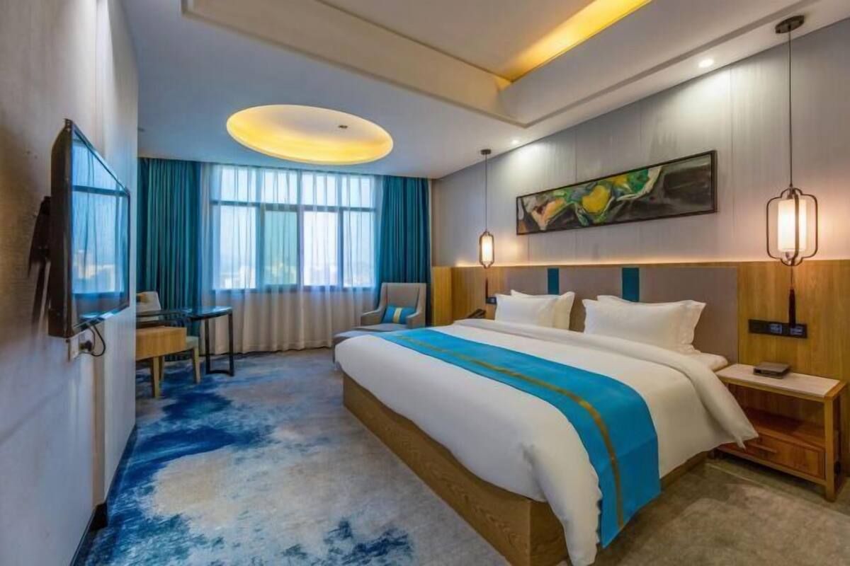 A hotel room with a large bed, a desk, a chair, a TV, and a painting on the wall.