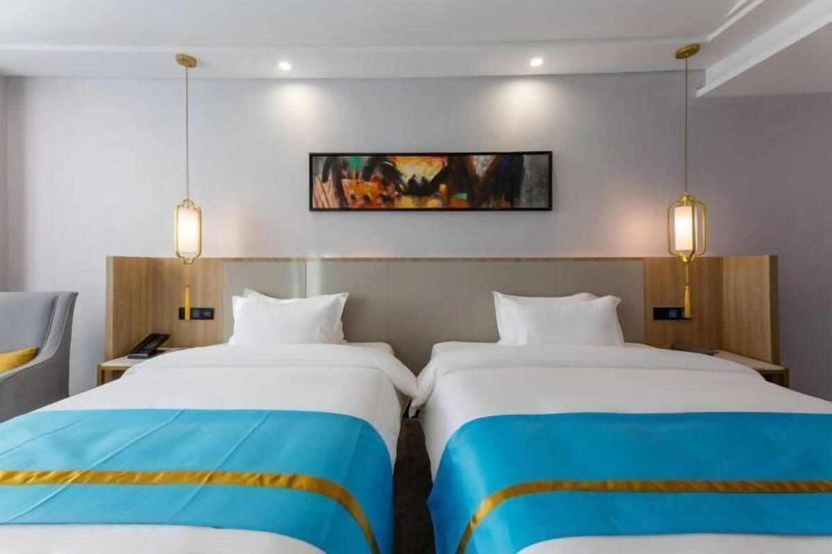 A hotel room with two beds, a painting on the wall, and pendant lights.