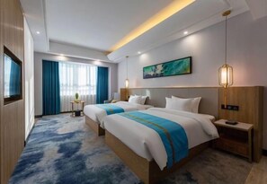 A hotel room with two beds, a large window with curtains, a painting on the wall, and a small table with a lamp. - Good China City International Hotel (Xingan)