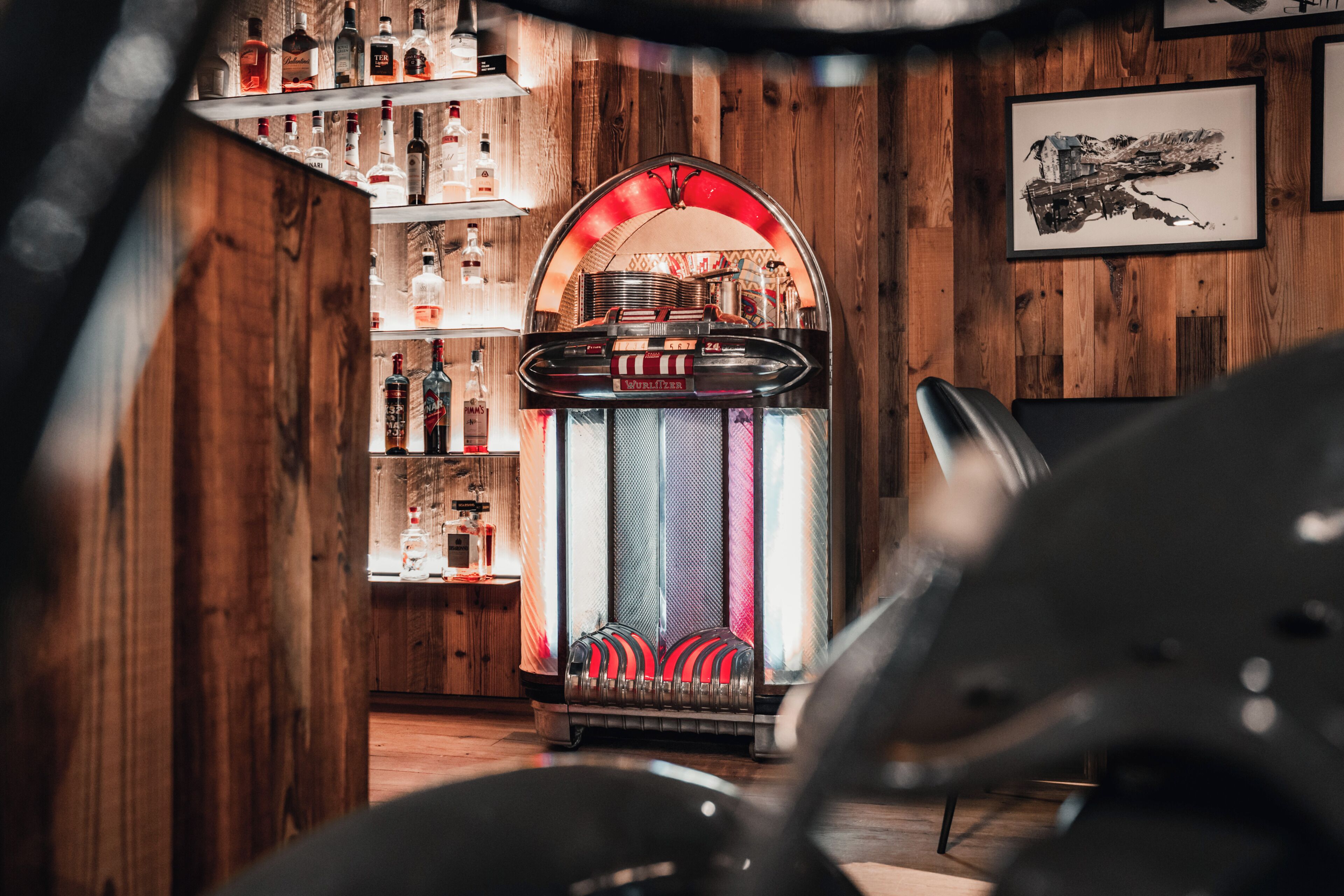Una habitación con paredes de madera, un jukebox, estantes con botellas y un cuadro enmarcado en la pared.