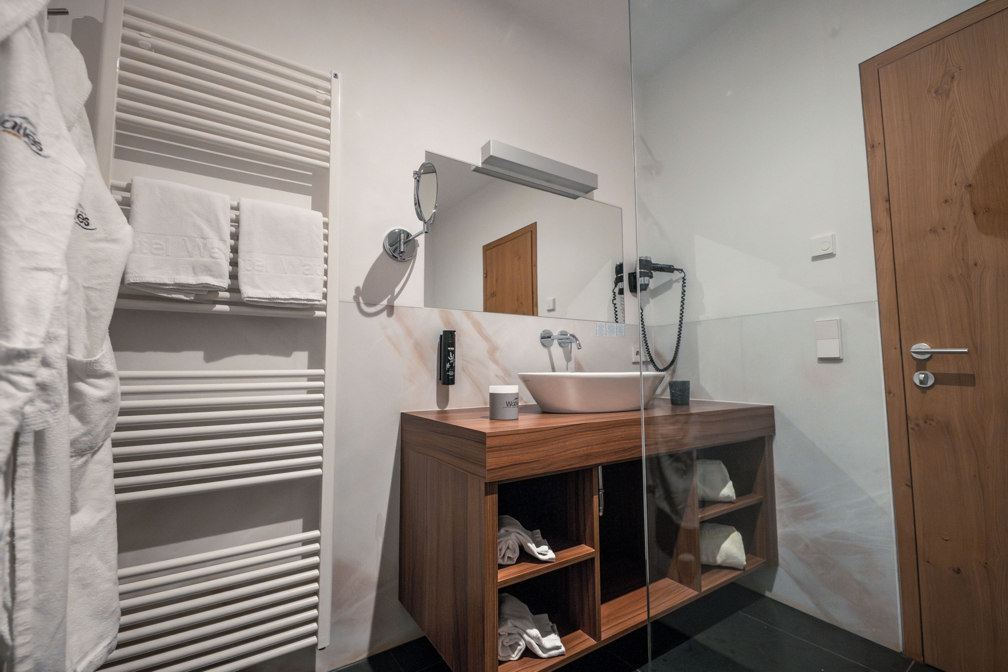 Un baño moderno con tocador de madera, un espejo grande, un lavabo blanco y un perchero para toallas.