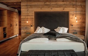 Une chambre à coucher avec une tête de lit en bois, un lit recouvert de draps blancs, un pied de lit foncé et deux lampes de chevet.