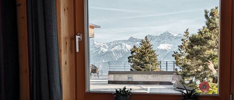 Mesa de comedor para dos personas con vistas a la montaña a través de una ventana, paredes de madera y un banco de cuadros.