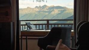 A room with a view of mountains, a wooden desk, a chair, and a hanging light fixture. - Panoramahotel Watles (Malles Venosta)