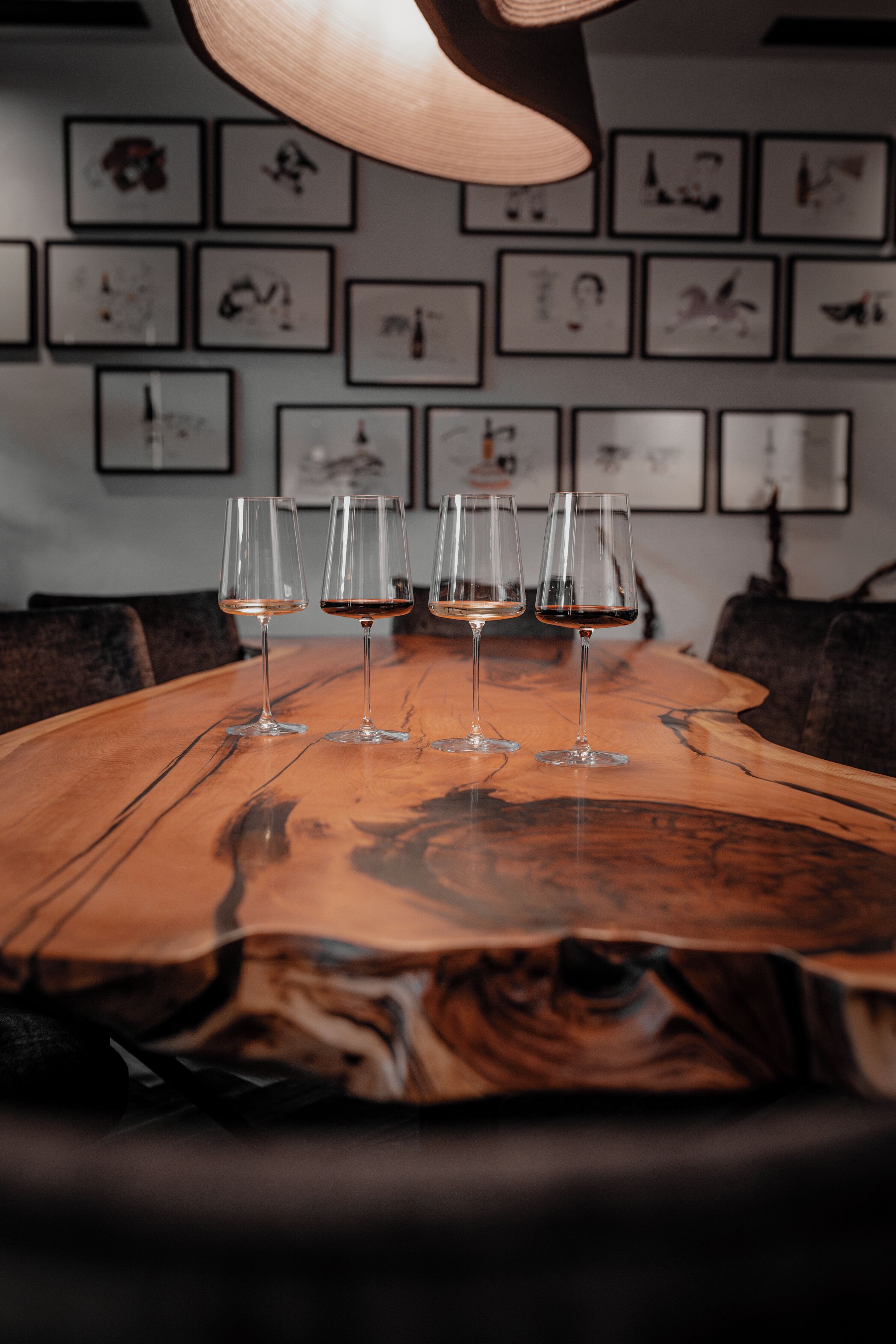 Een houten tafel met vier wijnglazen, een hanglamp en lijstwerken aan de muur.
