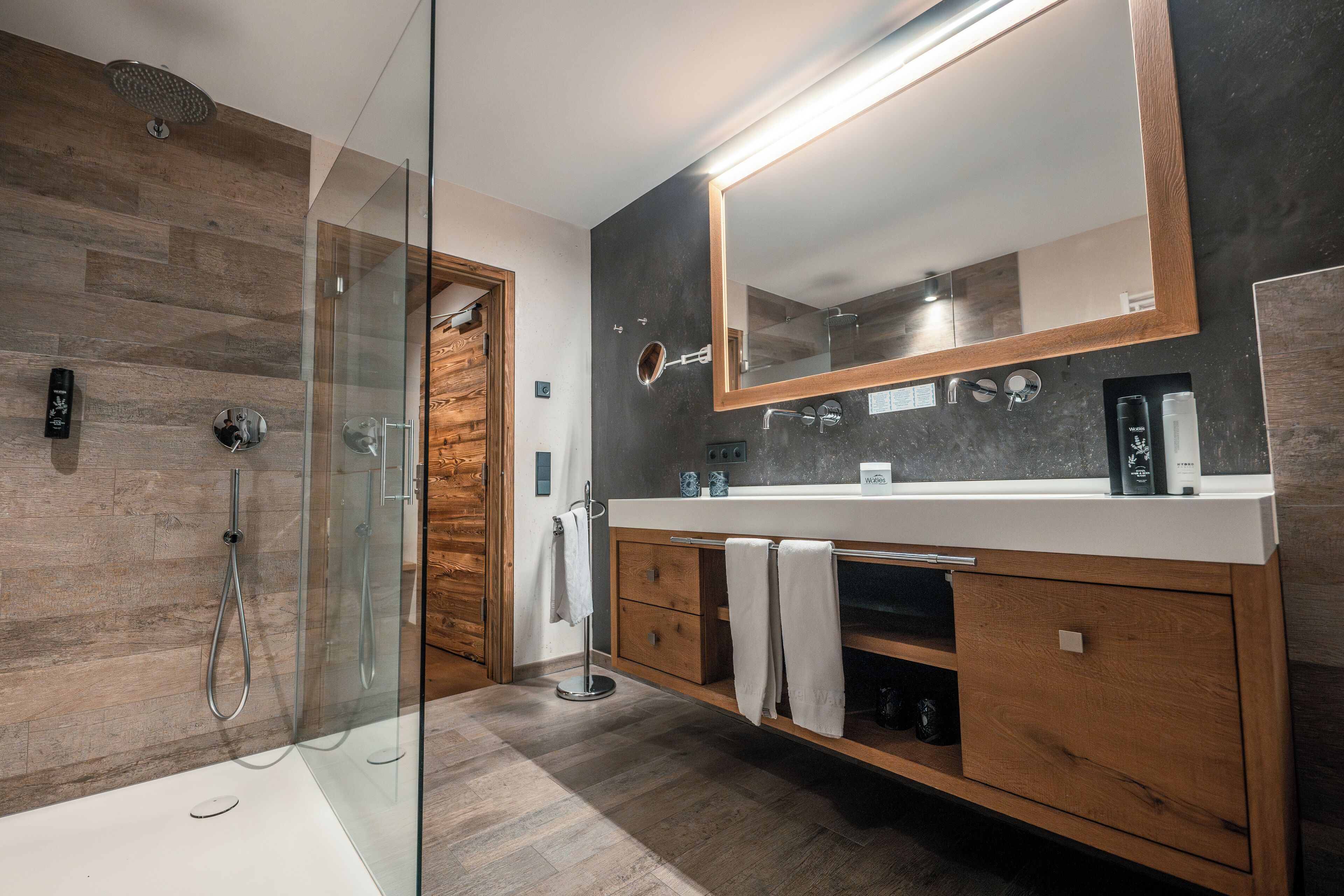 A modern bathroom with a glass-enclosed shower, wooden vanity, and a large mirror.