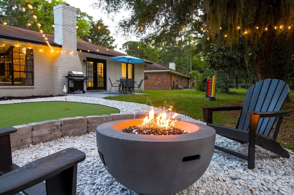 Un patio trasero con una chimenea, mobiliario exterior y una casa con porche cubierto.