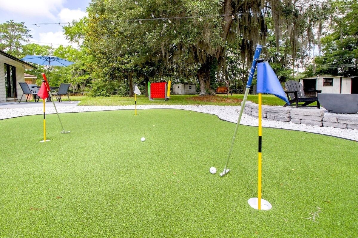 Ein Minigolfplatz mit grünem Kunstrasen, einer roten und gelben Fahne und einer kleinen Werkstatt im Hintergrund.