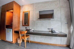 A hotel room with a wooden cabinet, a small refrigerator, a desk with a chair, a flat-screen TV mounted on the wall, and a trash bin. - J4 Samui Hotel (Koh Samui)