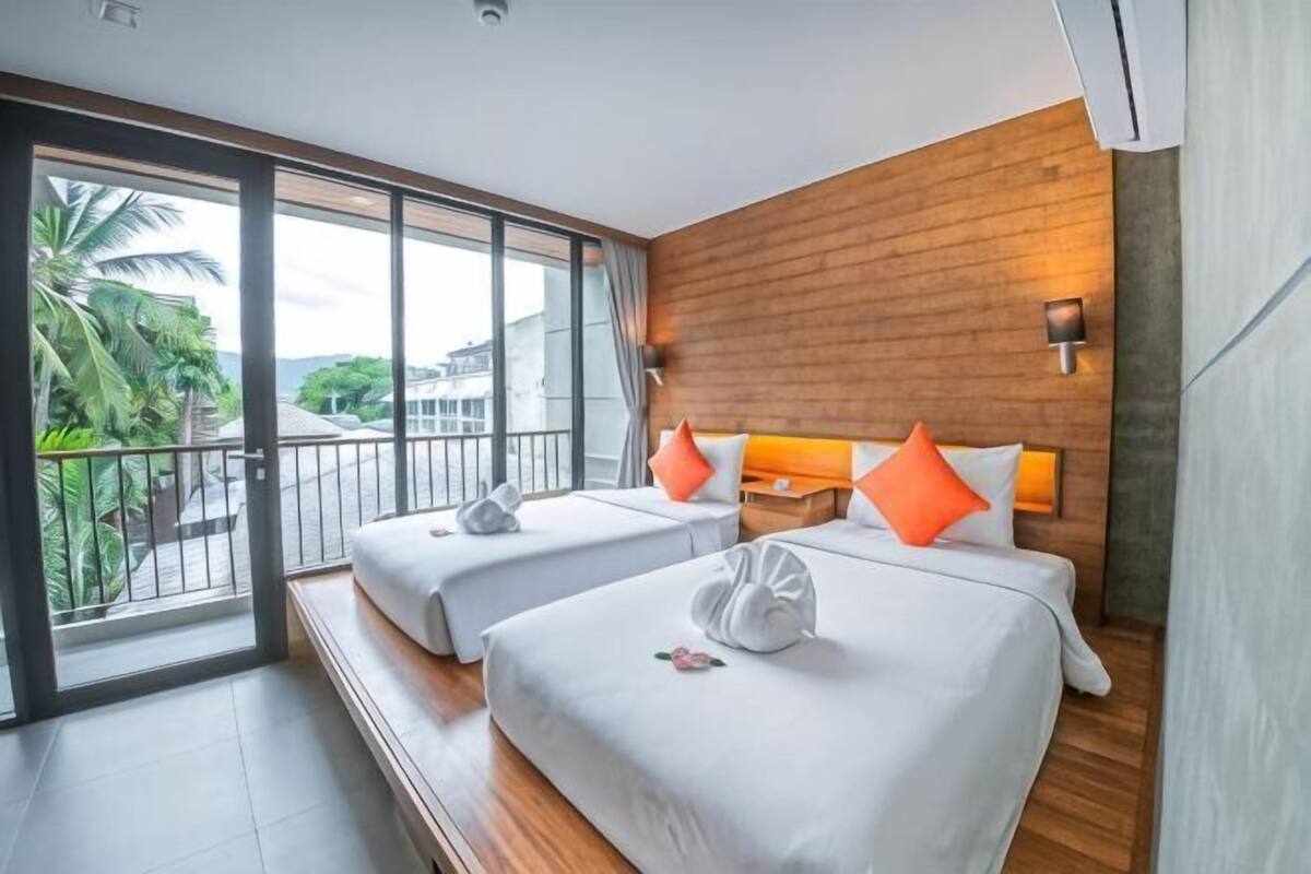 A hotel room with two beds, a balcony, and a view of palm trees.