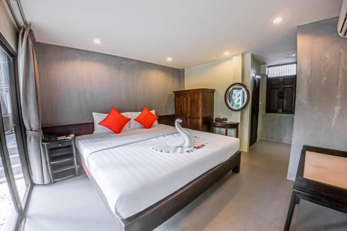 A hotel room with a bed, pillows, a wooden cabinet, a round mirror, and a window with curtains.