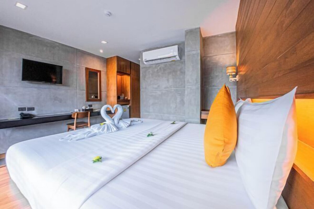 A modern hotel room with a large bed, a flat-screen TV, a wooden headboard, and a built-in desk.