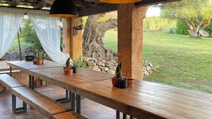 An outdoor dining area with wooden tables and benches, potted plants, and a view of a grassy landscape. - Masia Cal Mingo, paradise lost between vineyards and the sea, Barcelona Spain.   (Sant Miquel d'Olerdola)